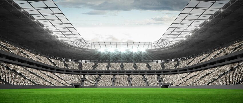 Flat green grass football pitch is extending under roof canopy with floodlights against cloudy sky