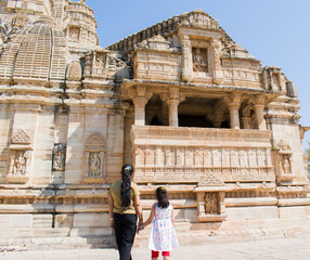 Rear view of a young Indian mother with her daughter posing in front of a historic temple inside...