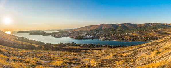 Panoramic aerial view of Grebastica near Sibenik, Croatia, captured at sunset with warm golden light illuminating the bay, and tranquil Adriatic waters along the scenic Dalmatian coastline