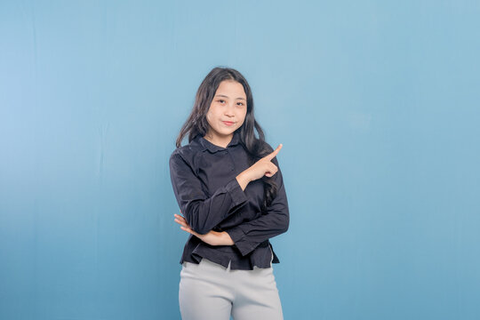 A woman is pointing at something with her finger. She is wearing a black shirt and white pants. She is smile and happy