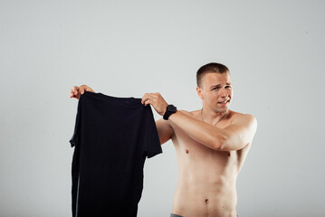 Disgusted Shirtless Man Holding T-Shirt With Uneasy Expression