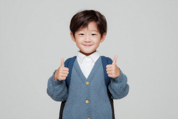 primary school kid with a backpack and thumbs up on neutral studio background