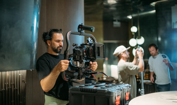 Director of photography with a camera in his hands on the set. Professional videographer at work on filming a movie, commercial or TV series. Filming process indoors, studio