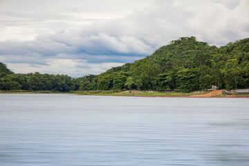 A peaceful rural scene in the dam featuring a yellow meadow and green mountain with blue sky, Chachoengsao, Thailand.