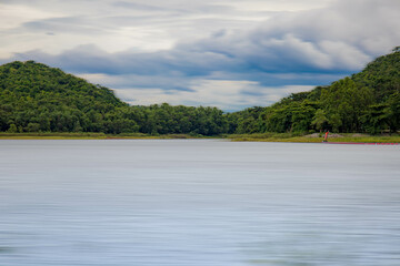A peaceful rural scene in the dam featuring a yellow meadow and green mountain with blue sky, Chachoengsao, Thailand.