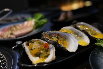 Silver platter filled with fresh, raw oysters on ice. Three bright yellow lemons are nestled among the oysters. High quality photo