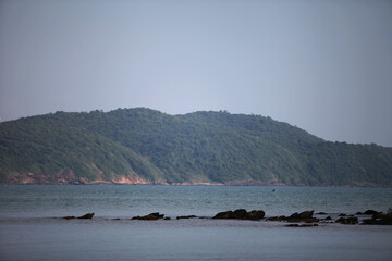 Tranquil Seaside Vista: Serene coastal panorama, capturing the expansive sea, rugged shoreline, and distant, lush hills under a serene, overcast sky.
