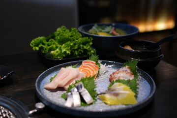 A vibrant Japanese sashimi salad featuring mixed raw fish, lettuce, and tomato, served on a textured ceramic plate with a dark background. High quality photo