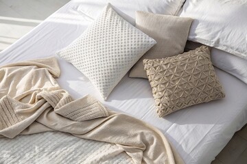 Cozy neutral bedding with textured pillows and blanket
Minimalist bed with cream and beige textured pillows and soft knitted blanket in natural light, evoking comfort and Scandinavian interior style.
