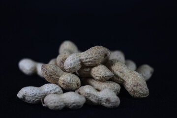 Peanuts on Black: A rustic pile of unpeeled peanuts, still in their shells, rests against a backdrop, showcasing their texture and raw appeal.