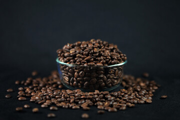 Coffee Beans: An artistic shot of a bowl of roasted coffee beans overflowing onto a dark surface, inviting you into the rich world of coffee, aroma and freshness.