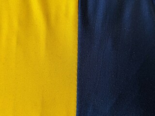 A close-up texture of yellow and dark blue fabric sewn together. A bold, two-tone color background...