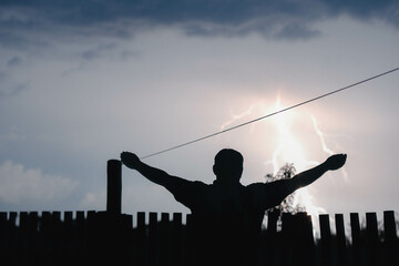 Silhouette of a person with outstretched arms against a stormy sky with a bright lightning strike.
