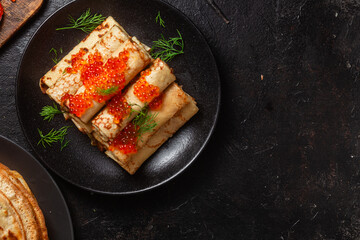 Delicious blini with red caviar in a black plate on the table. Thin pancakes. 