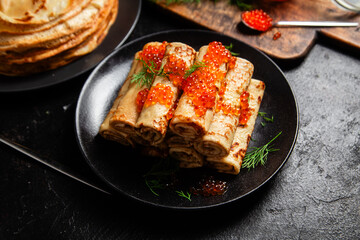 Delicious blini with red caviar in a black plate on the table. Thin pancakes. 