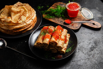 Delicious blini with red caviar in a black plate on the table. Thin pancakes. 