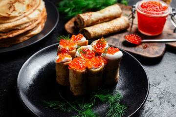 Delicious blini with red caviar in a black plate on the table. Thin pancakes. 