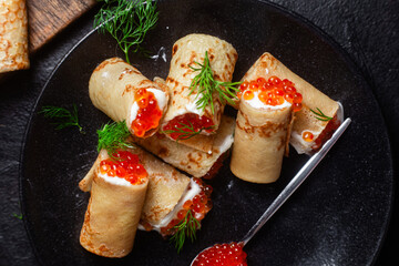 Delicious blini with red caviar in a black plate on the table. Thin pancakes. 