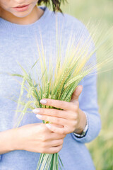 A young girl in a blue sweater holds a bunch of green wheat in her hands, symbolizing the...