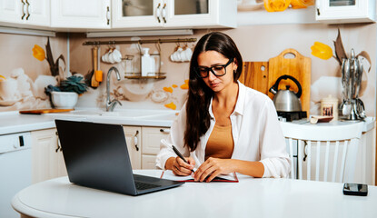 Woman writing in journal during online psychotherapy session at home. Mental health support,...