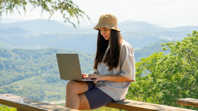 Young woman working on a laptop outdoors in the mountains. Digital nomad lifestyle, remote work in nature, summer freedom and productivity - Powered by Adobe