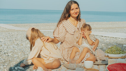 Young mother with children having a summer picnic by the sea, enjoying family time on the beach...