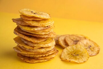 Stacked Fried Plantain Chips on Yellow Background – Crispy Tropical Snack Food Concept.