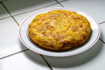 Homemade Spanish omelette served on a plate over a white tiled kitchen counter