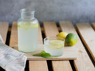 Glass bottle and glass with refreshing lemonade, wooden table, natural light and summer ingredients