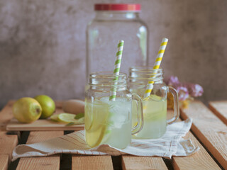 Glasses with handle with refreshing lemonade, ice, and lime and lemon wedges. Drink dispenser at...
