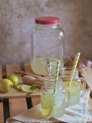 Glasses with handle with refreshing lemonade, ice, and lime and lemon wedges. Drink dispenser at the bottom