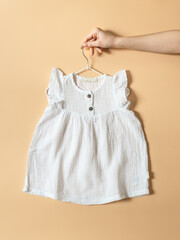 Hand is holding hanger with baby dress for girl. Clothing production, sewing workshop
