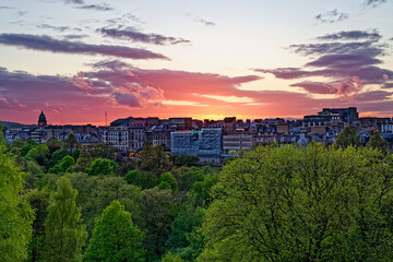 Fototapeta premium Beautiful sunset with orange pink sky above buildings on Princess street in Edinburgh, UK. Colorful sky with clouds. Above public park with green trees. Edinburgh, UK, 05.04.2025