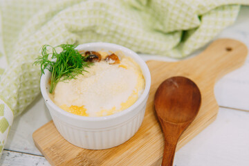 A delicious baked dish served in a white ramekin, garnished with fresh dill, resting on a wooden...