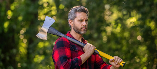 Lumberjack men in forest with axe. Lumberjack carries axe. Handsome man with axe. Lumberjack in woods with an ax. Lumberjack in shirt with heavy axe. Strong man work in forest. Focused expression