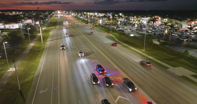 Nighttime traffic stop on USA city street as police pull over speeding vehicle. Patrol car lights flash in urban traffic environment.