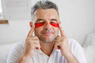 Middle Aged Man with Red Hydrogel Face Patches Relaxing and Enjoying Skincare Routine at Home