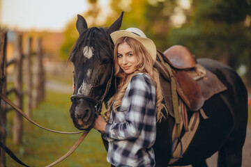 A young woman with a horse stands near a fence in autumn at sunset. Breeding thoroughbred horses for equestrian sport.