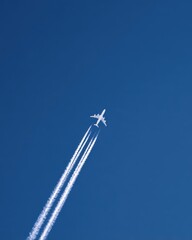 Airplane Flying High in Clear Blue Sky with Contrails Streamers Leaving Behind in the Daytime