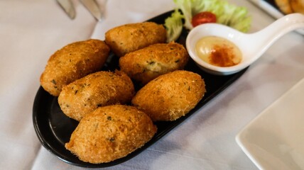 close up of six pieces of Bacalhau fritters ( fried salted cod fritters) a traditional food in Macau on a black palte