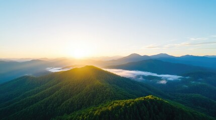 Obraz premium Sunrise over a mountain range. Lush green forested peaks are bathed in golden sunlight, with clouds clinging to the valleys. A tranquil and majestic scene