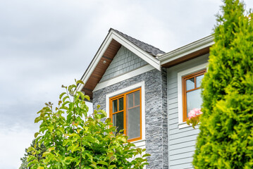 Top of grey stucco luxury house with shingle roof, green trees and nice windows in Spring in...