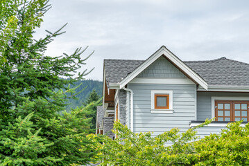 Top of grey stucco luxury house with shingle roof, green trees and nice windows in Spring in Vancouver, Canada, North America. Day time on May 2025.