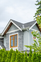 Top of grey stucco luxury house with shingle roof, green trees and nice windows in Spring in Vancouver, Canada, North America. Day time on May 2025.