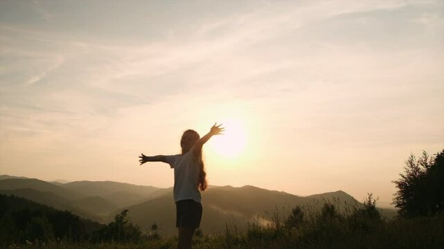 Dreaming happy child outstretching arms up on background mountains. Preteen girl enjoy warm sunset, enjoying rest at nature. Freedom emotion and flying thoughts