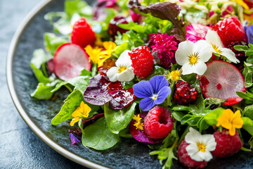 Bright gourmet summer salad with edible flowers, raspberries, tomatoes and greens for fresh healthy vegan seasonal meals