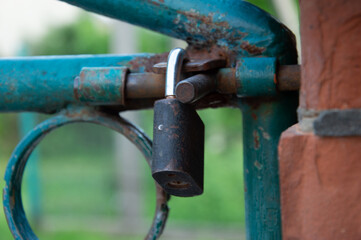 A rusty padlock is securing an old blue gate, surrounded by lush greenery in a tranquil park on a sunny afternoon