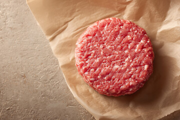 Raw ground beef meat shaped in a circle for burger patty, on wax paper. Kitchen counter background,
