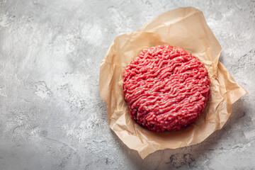 Raw ground beef meat shaped in a circle for burger patty, on wax paper. Kitchen counter background,
