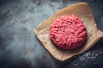 Raw ground beef meat shaped in a circle for burger patty, on wax paper. Kitchen counter background,

